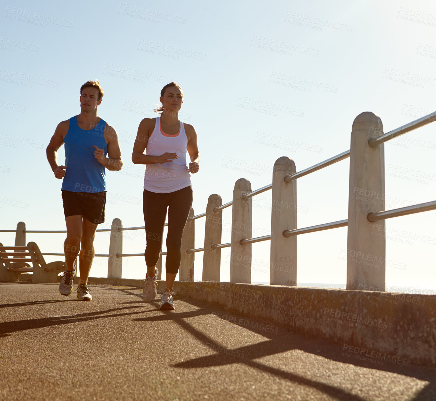 Buy stock photo Shot of a young couple jogging together the promenade 