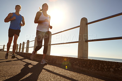 Buy stock photo Shot of a young couple jogging together the promenade 