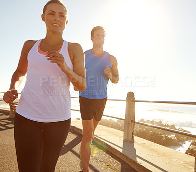 Buy stock photo Shot of a young couple jogging together on the promenade 
