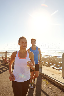 Buy stock photo Shot of a young couple jogging together on the promenade 