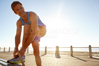 Buy stock photo Shot of an athletic man tying his shoe laces on a bench 