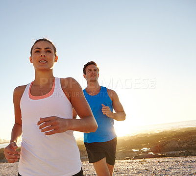 Buy stock photo Shot of a young couple jogging together by the beach