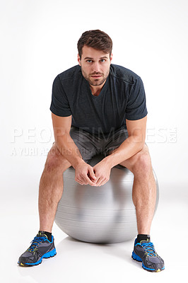 Buy stock photo Studio shot of a serious young man sitting on an exercise ball