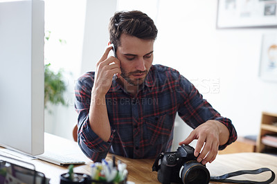 Buy stock photo Shot of a photographer talking on the phone while looking at his camera