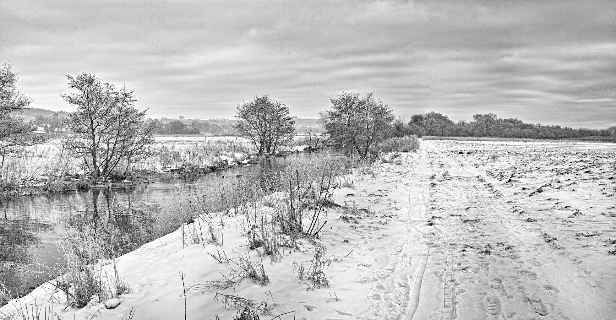 Buy stock photo A black and white view of a mountain lake in winter, covered with snow and ice. The beautiful cloudy weather around the pond covered with snowfall. A dense forest and cloudy sky on a glacial valley.