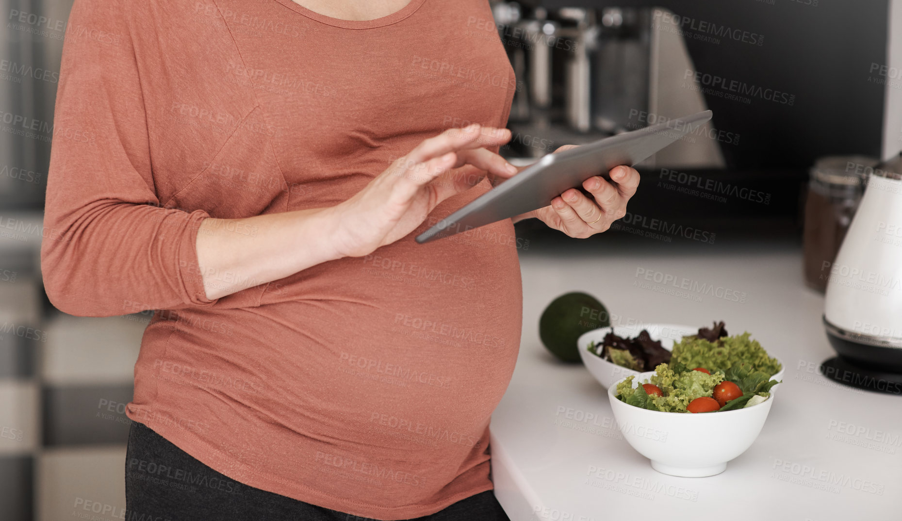 Buy stock photo Cropped shot of a pregnant woman using her tablet while eating a salad in the kitchen