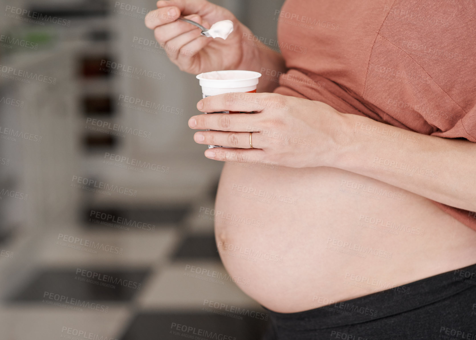 Buy stock photo Cropped shot of a young pregnant woman eating a yogurt in the kitchen