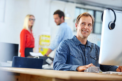 Buy stock photo Shot of a designer at work on a computer with colleagues in the background