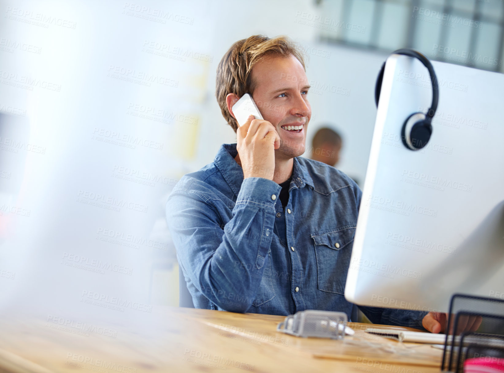 Buy stock photo Shot of a designer talking on a cellphone while working on a computer in an office