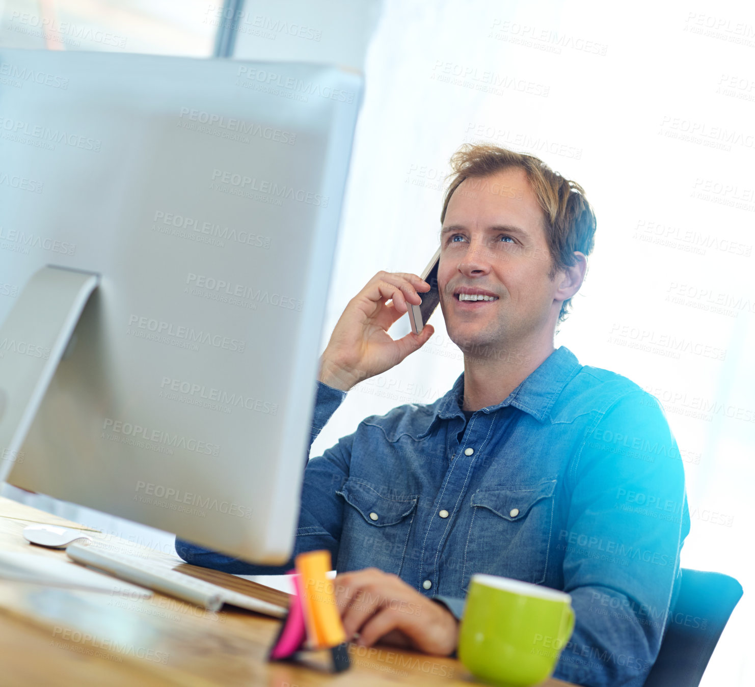 Buy stock photo Shot of a designer talking on a cellphone while working on a computer in an office