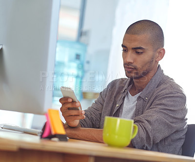 Buy stock photo Shot of a designer using a cellphone while working on a computer in an office