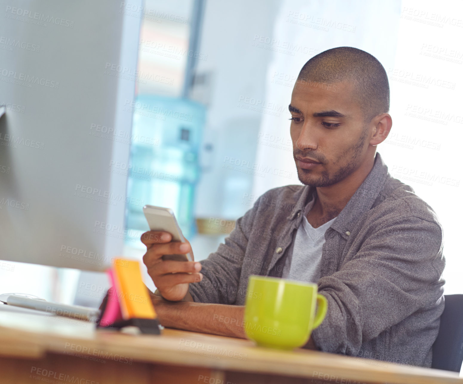 Buy stock photo Shot of a designer using a cellphone while working on a computer in an office