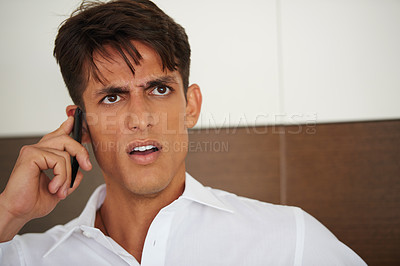 Buy stock photo Shot of a young businessman looking displeased while talking on the phone