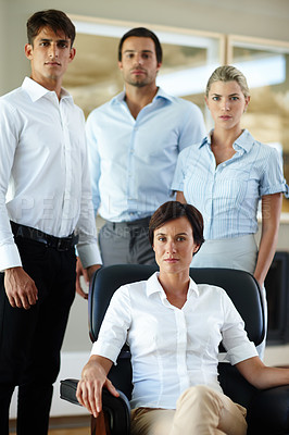 Buy stock photo Portrait of a serious business manager sitting in a chair with her team standing behind her