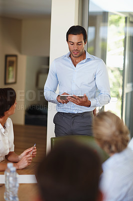 Buy stock photo Shot of a handsome businessman with a tablet delivering a presentation during a meeting