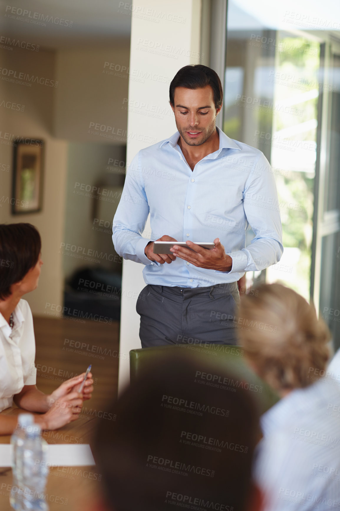 Buy stock photo Shot of a handsome businessman with a tablet delivering a presentation during a meeting