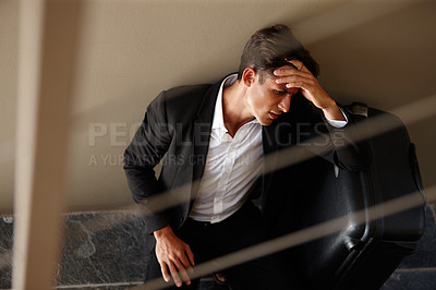 Buy stock photo Shot of an exhausted young businessman sitting on the floor beside his luggage