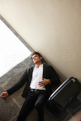 Buy stock photo Shot of an exhausted young businessman lying on the floor beside his luggage