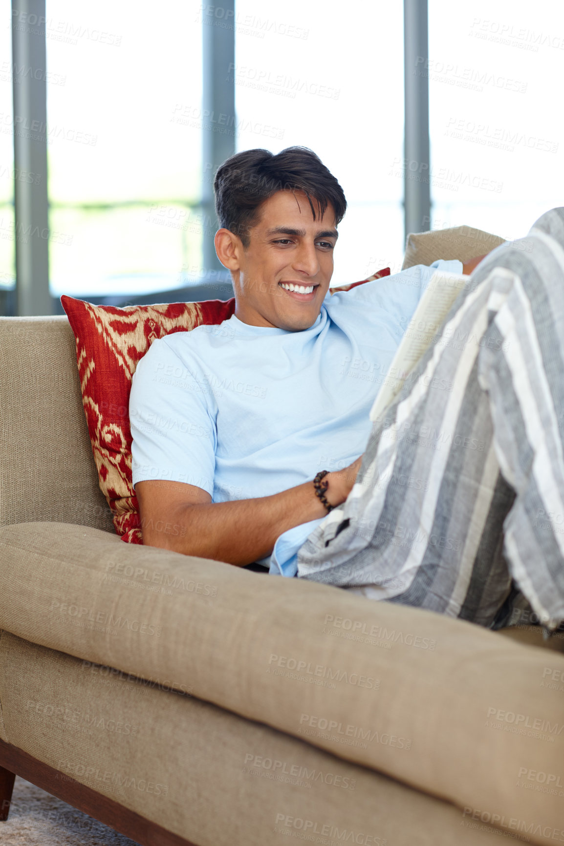 Buy stock photo Shot of a handsome young man sitting on his sofa while reading a book