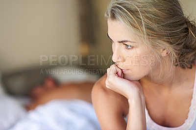 Buy stock photo Shot of a young woman deep in thought while her husband sleeps in the background