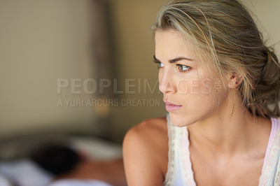 Buy stock photo Shot of a young woman deep in thought while her husband sleeps in the background