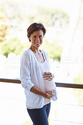 Buy stock photo Shot of a pregnant woman holding onto her tummy while standing on a balcony