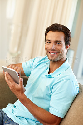 Buy stock photo Portrait of a handsome man using a digital tablet while sitting on the sofa at home