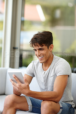 Buy stock photo Shot of a young man using a tablet while sitting on the sofa