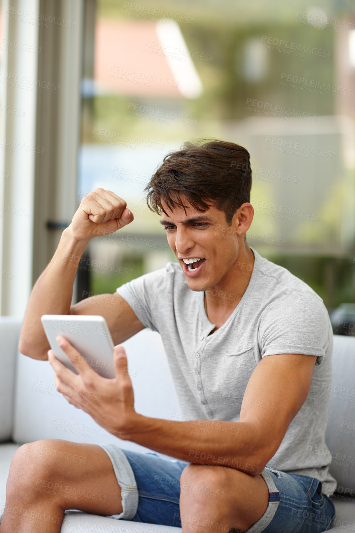 Buy stock photo Shot of a young man cheering while watching something on his tablet at home