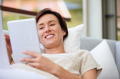 Buy stock photo Shot of an attractive woman using her tablet while lying on the sofa at home