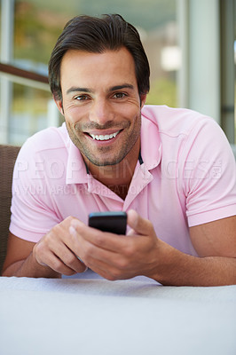 Buy stock photo Portrait of a handsome man using his cellphone while lying on the sofa at home