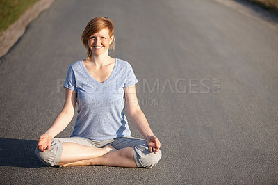 Buy stock photo Portrait of an attractive woman sitting in the lotus position on a road