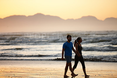 Buy stock photo Shot of a couple walking along a beach at daybreak