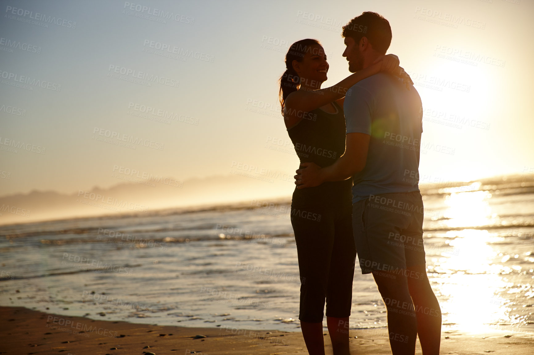 Buy stock photo Shot of a hugging couple silhouetted against a sunrise over the sea