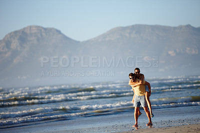 Buy stock photo Shot of a young man piggybacking his girlfriend on a beach