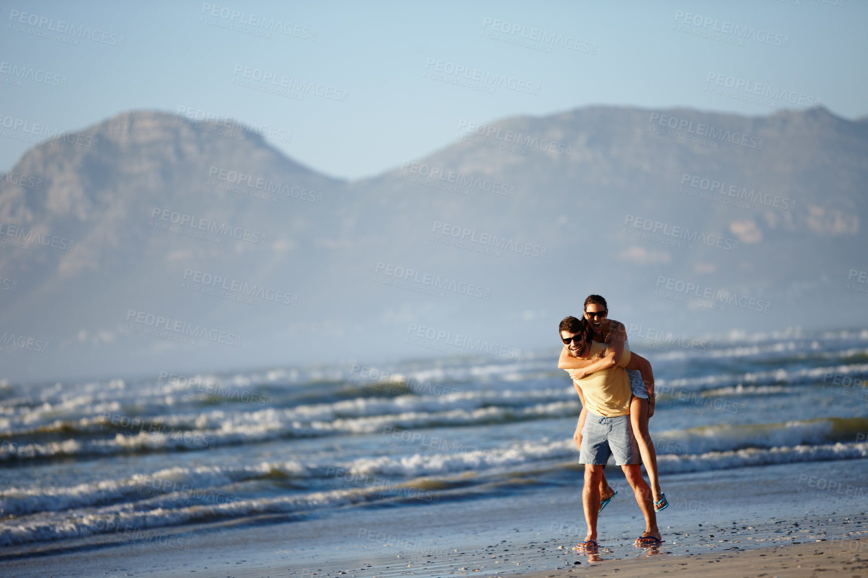 Buy stock photo Shot of a young man piggybacking his girlfriend on a beach