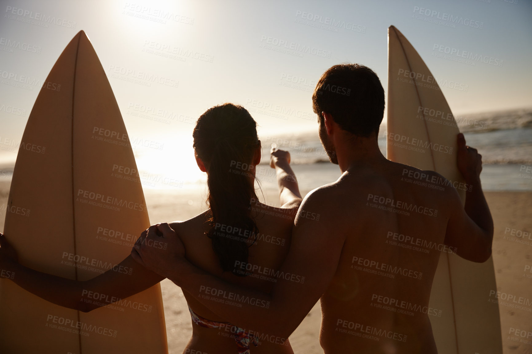 Buy stock photo Rearview shot of a young surfer couple looking out at the beach and distant waves