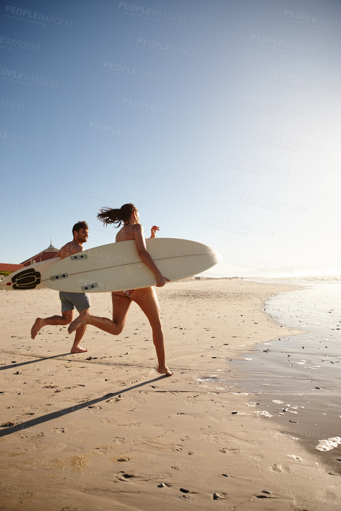 Buy stock photo Shot of a young surfing couple running along the shore with their surfboards
