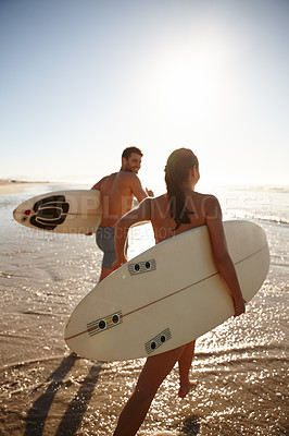 Buy stock photo Rearview shot of a young surfer couple running into the sea together