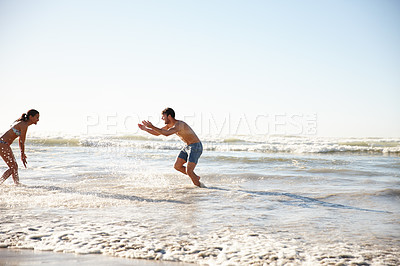 Buy stock photo Shot of a happy couple playing in the shallow water together on the beach