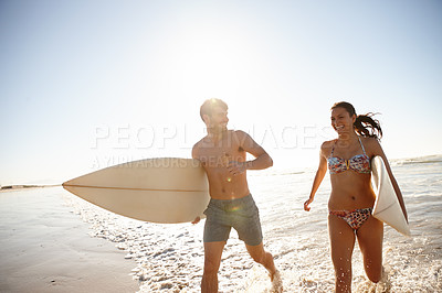 Buy stock photo Shot of a young couple running out of  the sea with their surfboards
