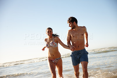 Buy stock photo Shot of a young couple running out of  the sea together holding hands