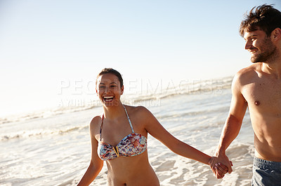 Buy stock photo Shot of a happy couple laughing while running out of the sea together