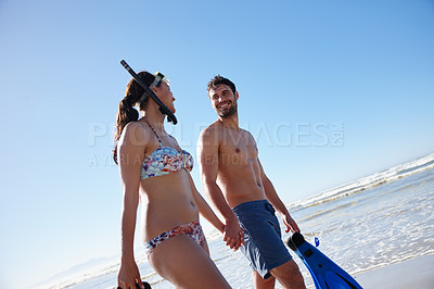 Buy stock photo Low angle shot of a young couple walking along a beach together with snorkeling gear