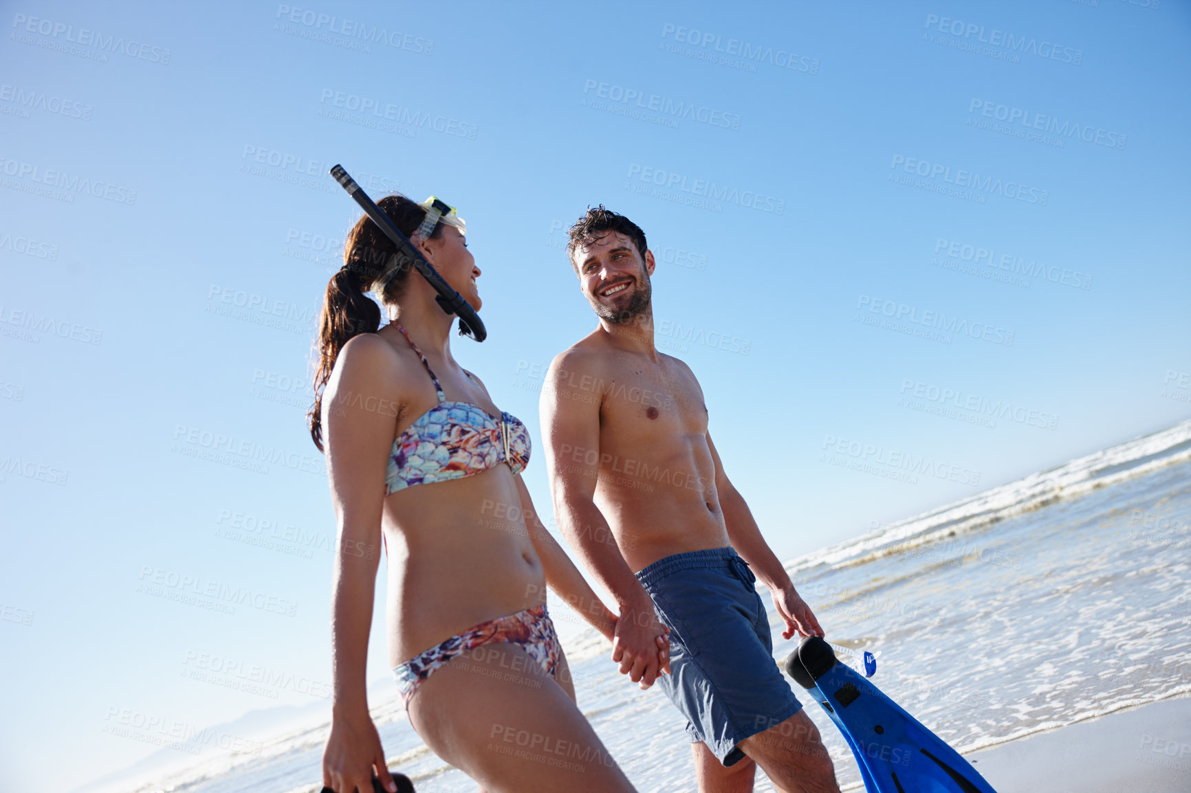 Buy stock photo Low angle shot of a young couple walking along a beach together with snorkeling gear