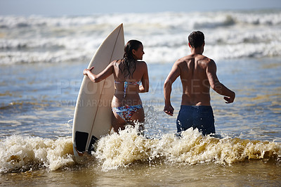 Buy stock photo Rearview of a young surfer couple walking into the waves together