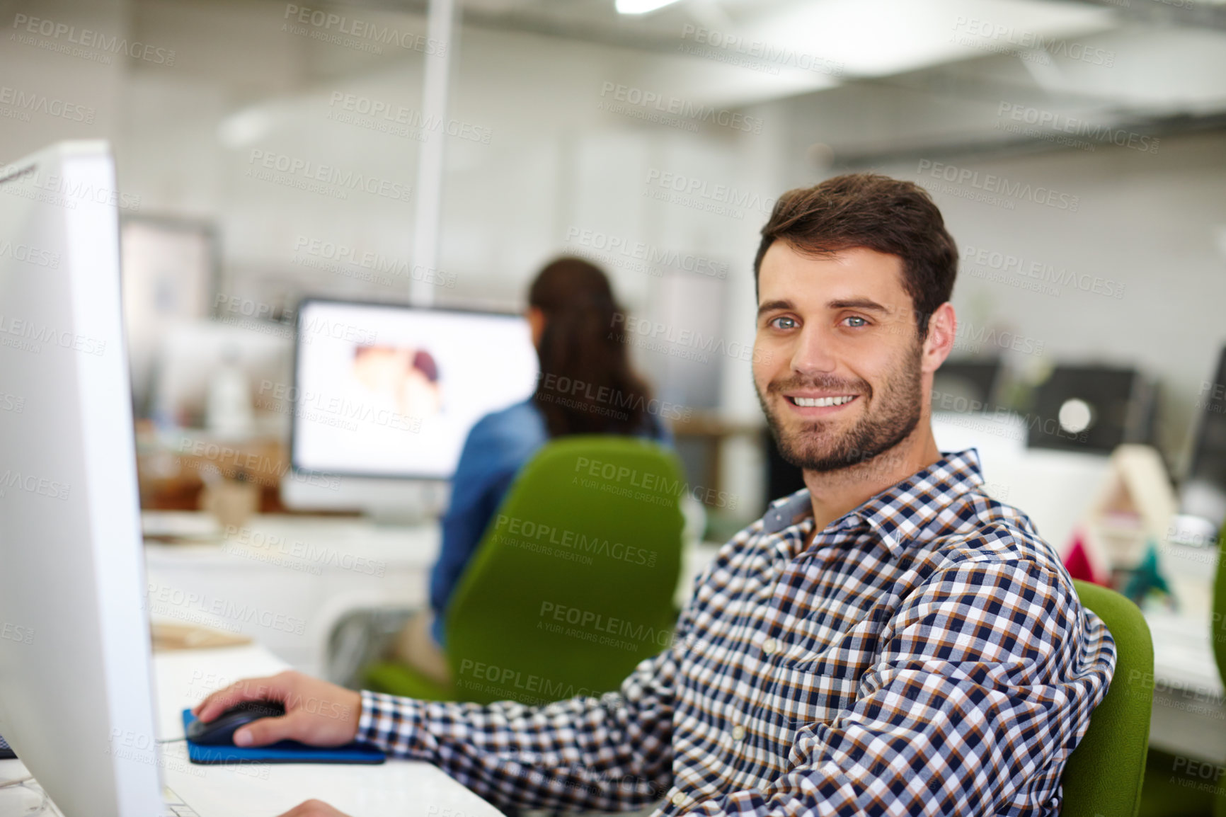 Buy stock photo Portrait of a handsome young designer sitting at his desk with a colleague in the background