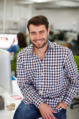 Buy stock photo Portrait of a handsome young designer sitting on his desk with a colleague in the background