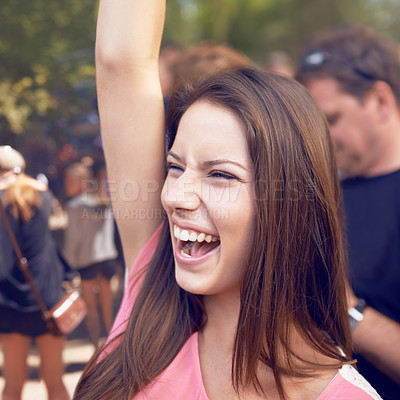 Buy stock photo A beautiful young woman smiling and enjoying music at a festival with arm raised in the air and crowd in the background