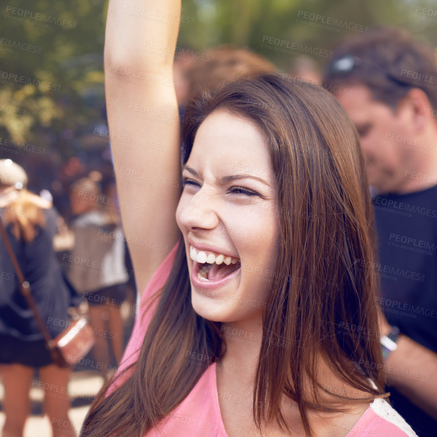Buy stock photo A beautiful young woman smiling and enjoying music at a festival with arm raised in the air and crowd in the background